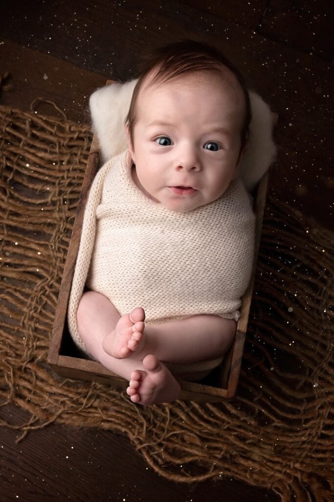Older newborn looking at camera wrapped in cream wrap