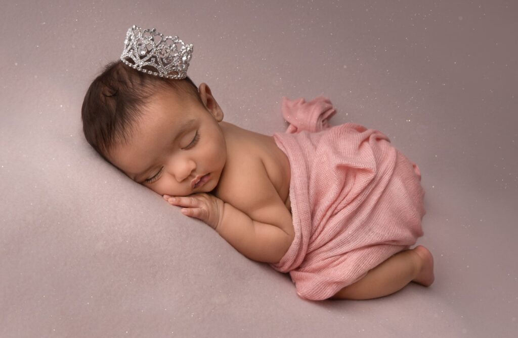 Older newborn wrapped in pink with crown on head