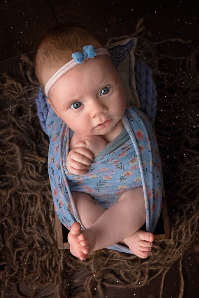 older newborn in wooden crate wrapped in blue