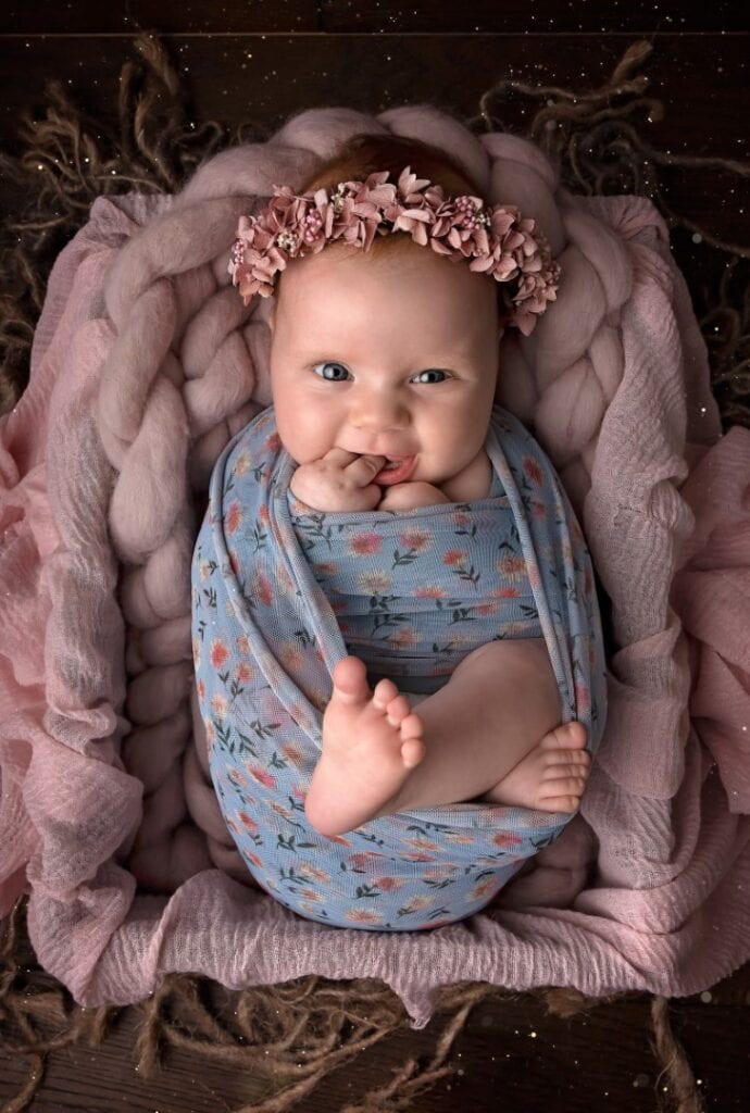 Older newborn wrapped in flower wrap with flower headband