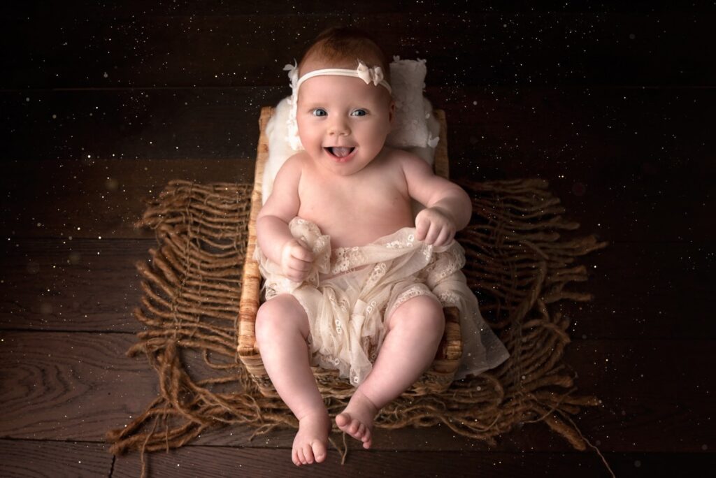 Older newborn in cream outfit sitting in wicker basket