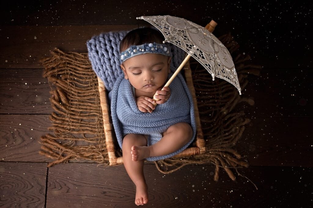 Older newborn in crate holding small umbrella